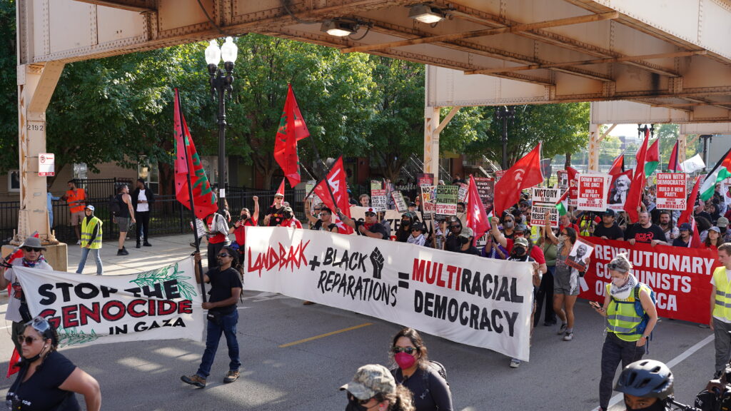 Photo description: Indigenous Peoples' at the March on DNC display a Landback + Black Reparations = Multiracial Democracy banner.