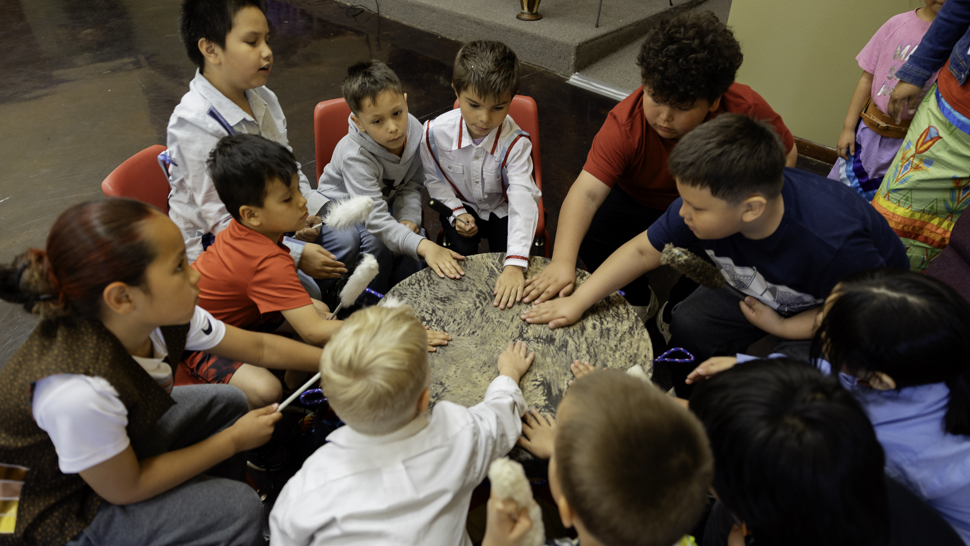 Native American students place their hands on a drum