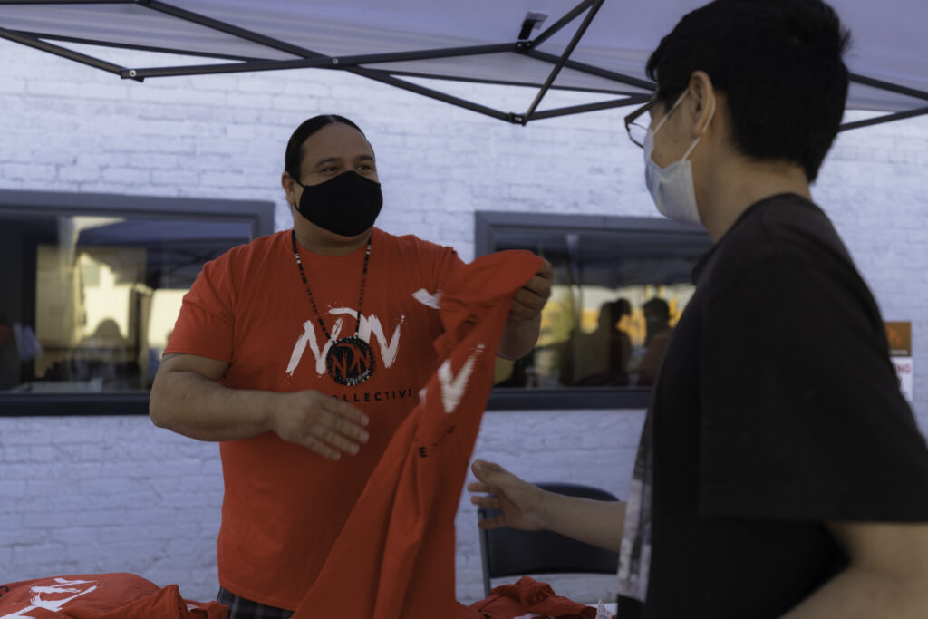 An image of a man handing a t-shirt that says "NDN Collective" to a young person.
