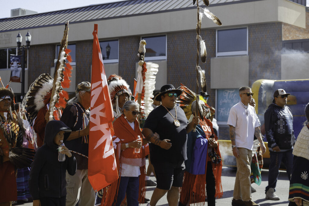 An image of Native Americans marching with flags that display the message "LANDBACKā during a local march.