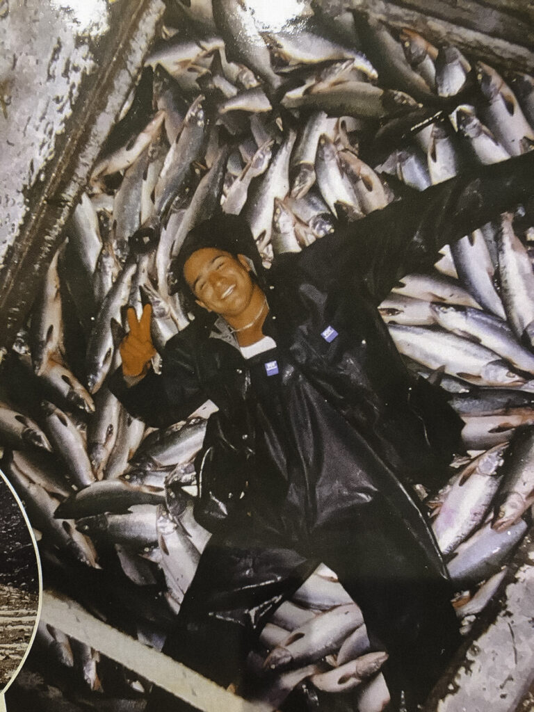 An image of a Native American man smiling and laying on top of fish in Cordova, AK.