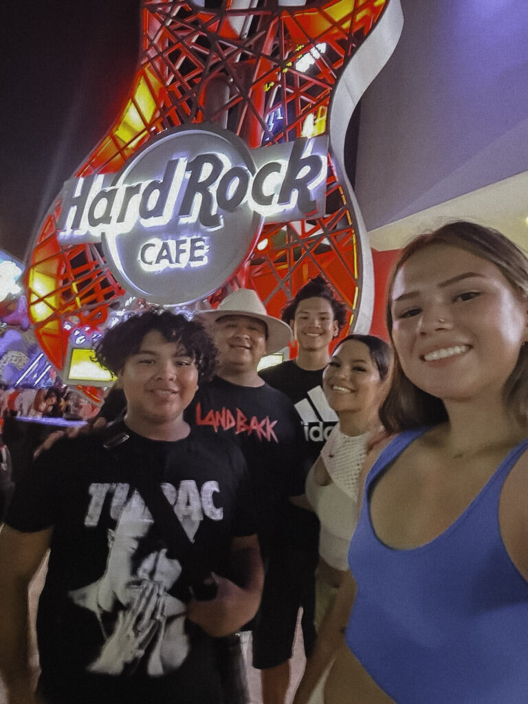 Image of a Native American dad taking a selfie with his four kids in front of the Hard Rock sign in Las Vegas, NV.