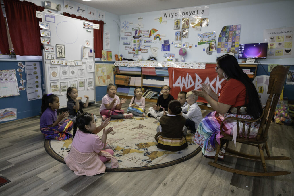 An image of students sitting in a circle, learning and following the teacher's instructions in a classroom.