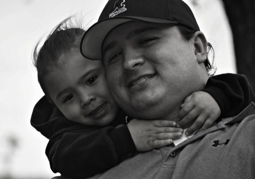 The image of Native American man and his son, both smiling at the camera.